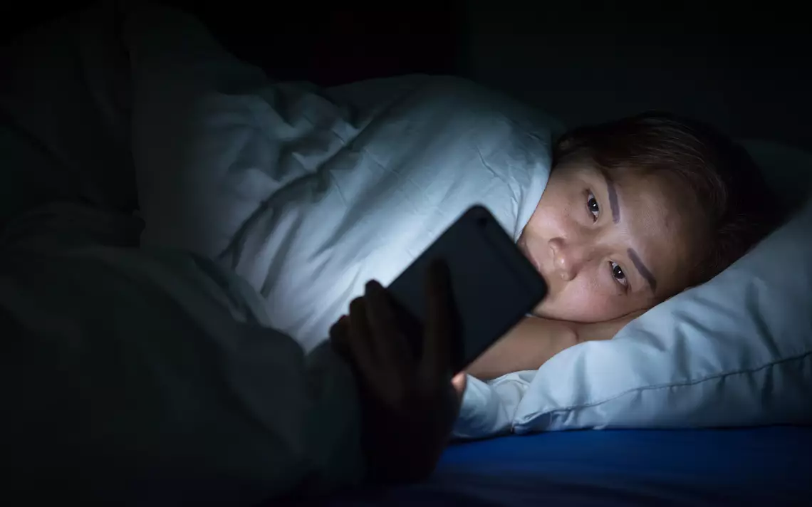 une adolescente qui consulte son smartphone dans son lit à des heures tardives