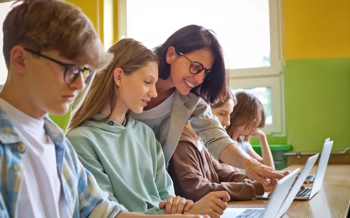 Un professeur et des enfants travaillant sur des ordinateurs.