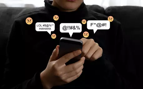 Un jeune tenant un smartphone d'où sortent des emojis négatives